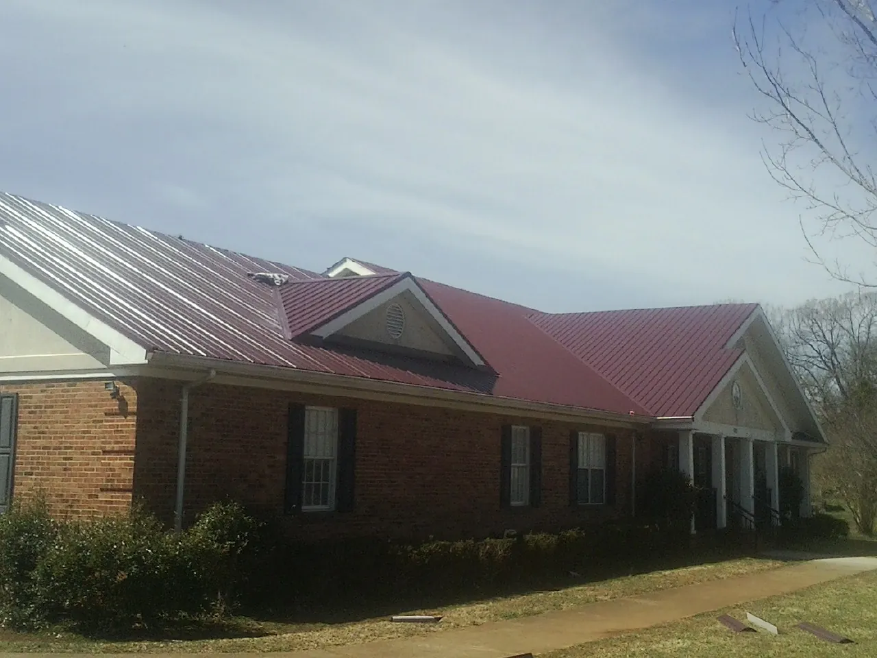 Red metal roof with gabled entries on a long brick building, from a Hail Damage Roof Repair job in West Union