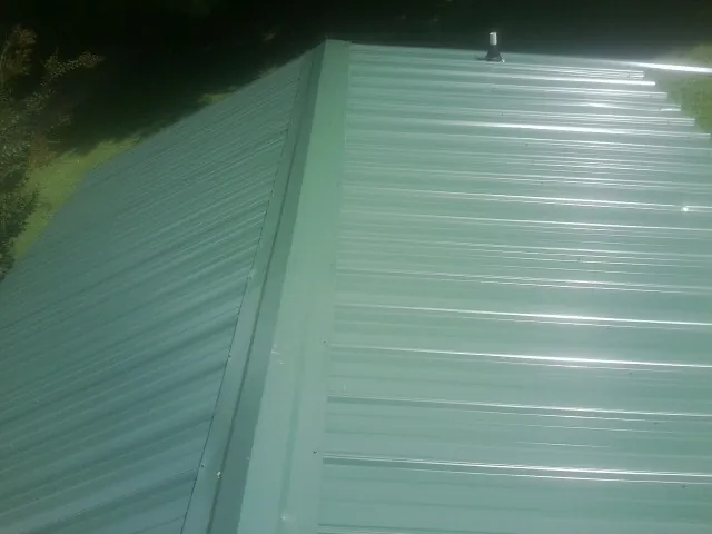 New green metal panels meeting at the ridge of a roof — Flat Roof Repair work by our crew in West Union