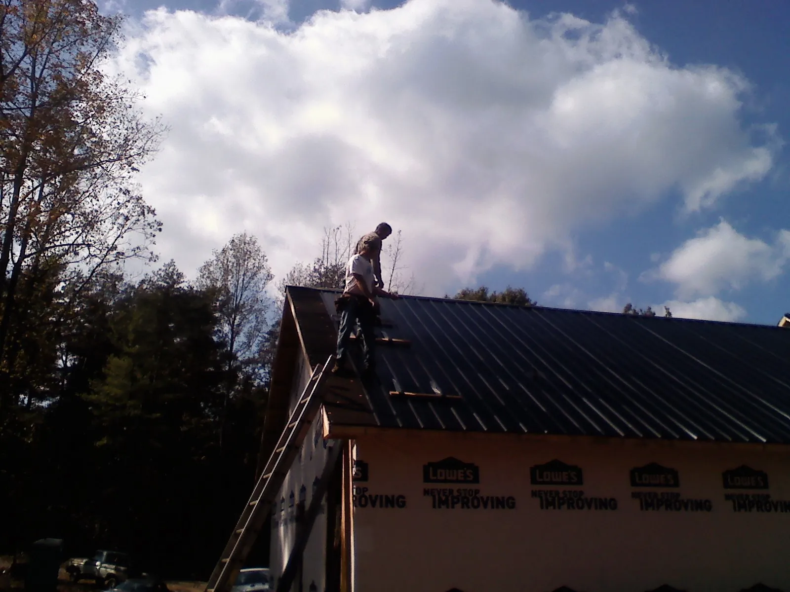 Roofer fastening dark metal panels high against a cloudy sky, from a Roof Inspection job in West Union