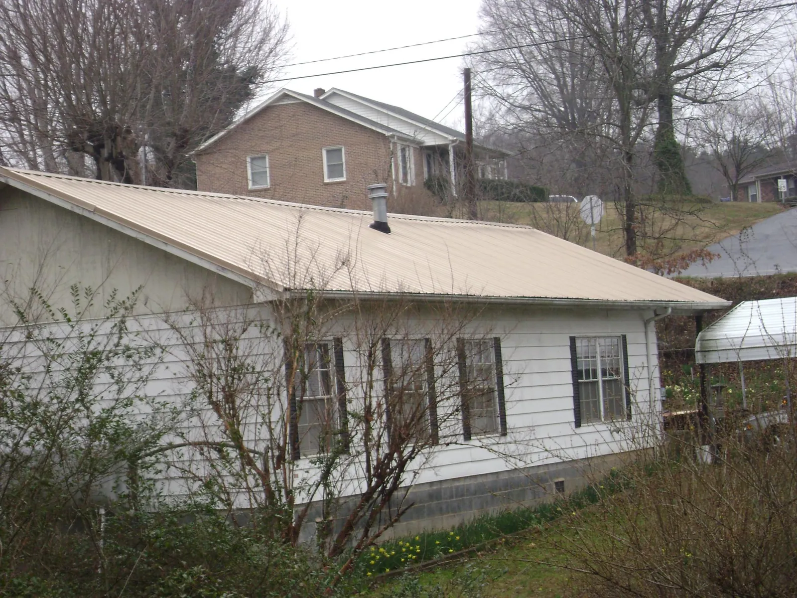 Tan metal roof on a white sided house set into a hillside — Commercial Roofing by Roofing Brothers in West Union